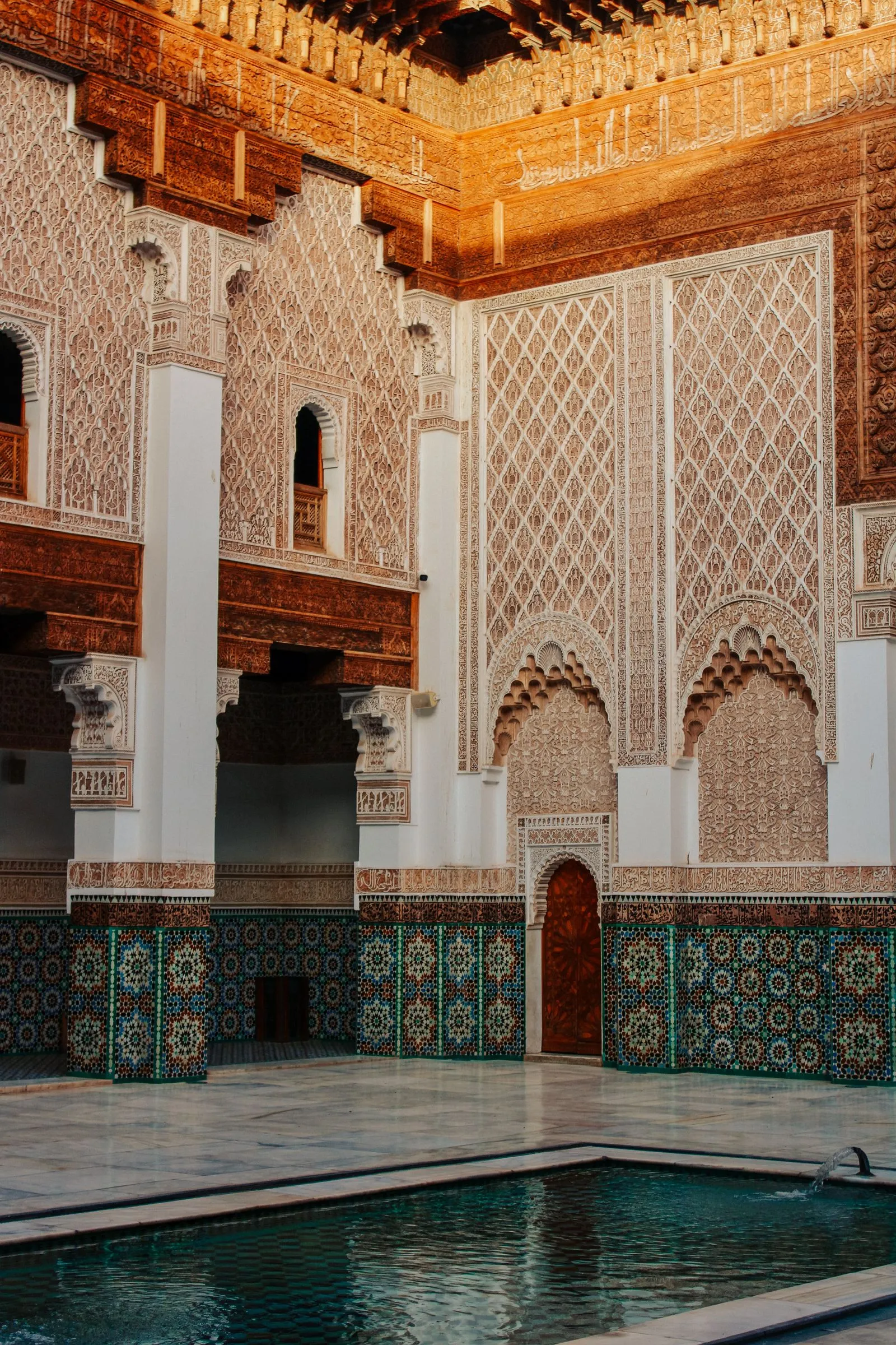Stucs sculptés, arcs et zellige de la médersa Ben Youssef à Marrakech, lumière ambrée
